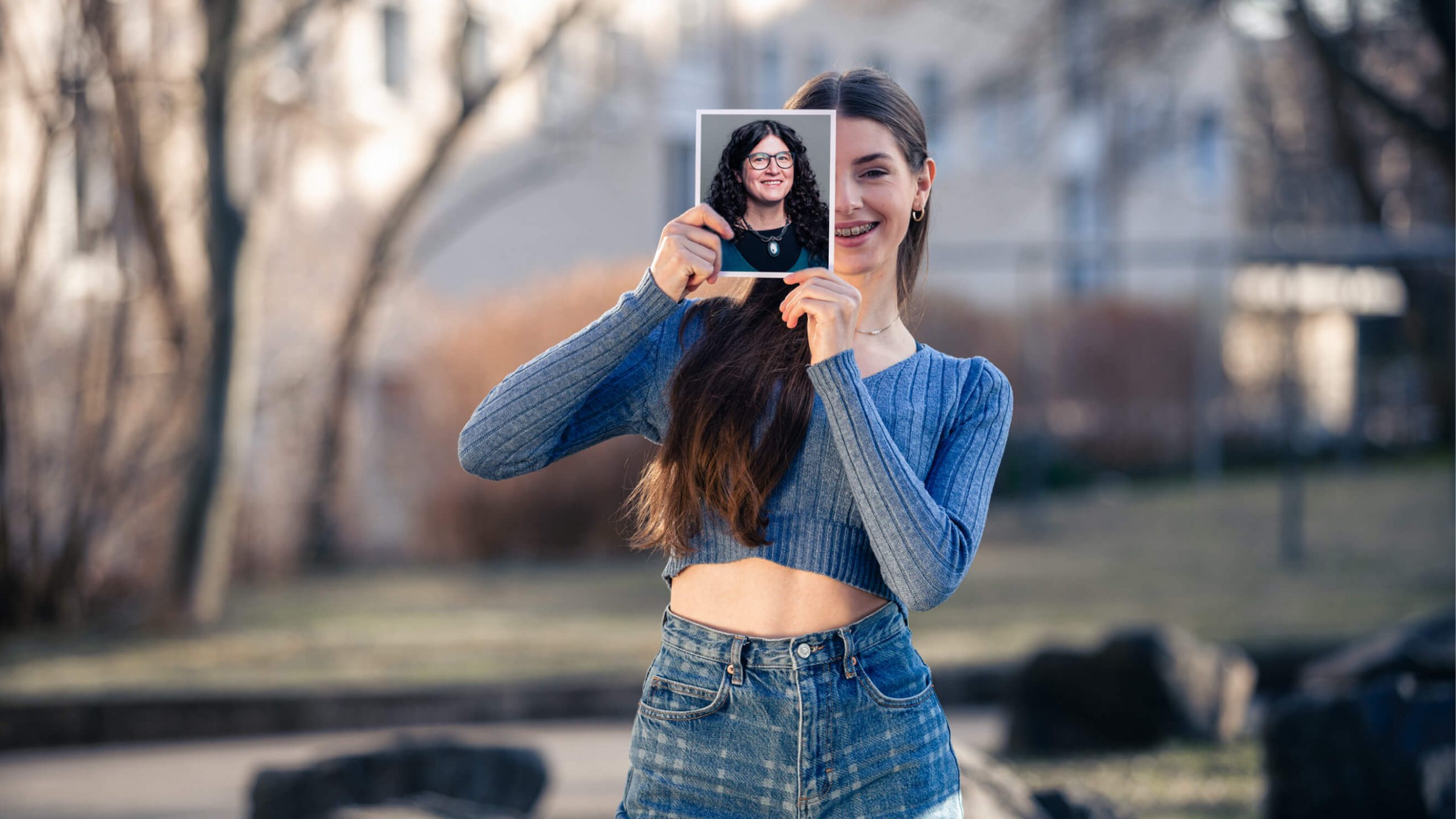 Eine Frau hält ein Foto von sich selbst in der Hand und lächelt dabei in die Kamera.