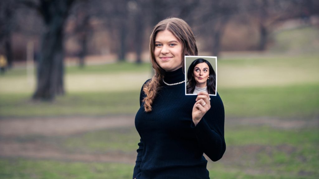 Eine Frau hält ein Foto mit einem Gesichtsausdruck in einer Parklandschaft in der Hand.