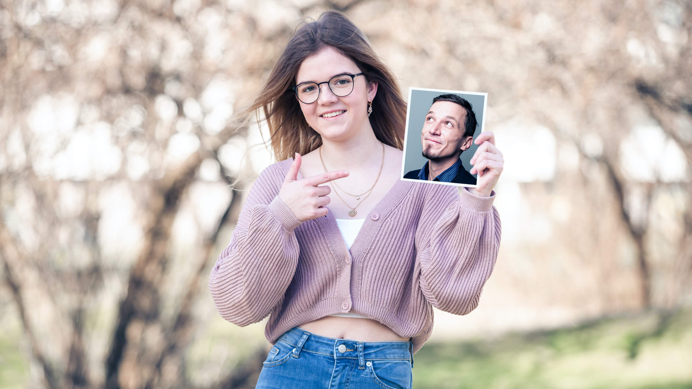 Eine junge Frau zeigt auf ein Foto eines Mannes, während sie im Freien steht.