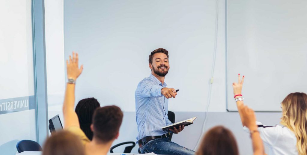 Lehrer, der im Klassenzimmer steht und auf Schüler zeigt, die ihre Hände heben.