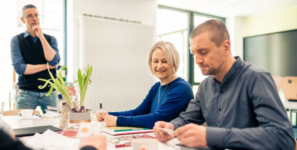 Eine Gruppe von Lehrern sitzt an einem Tisch in einem Besprechungsraum, während sie sich unterhalten und Notizen machen.