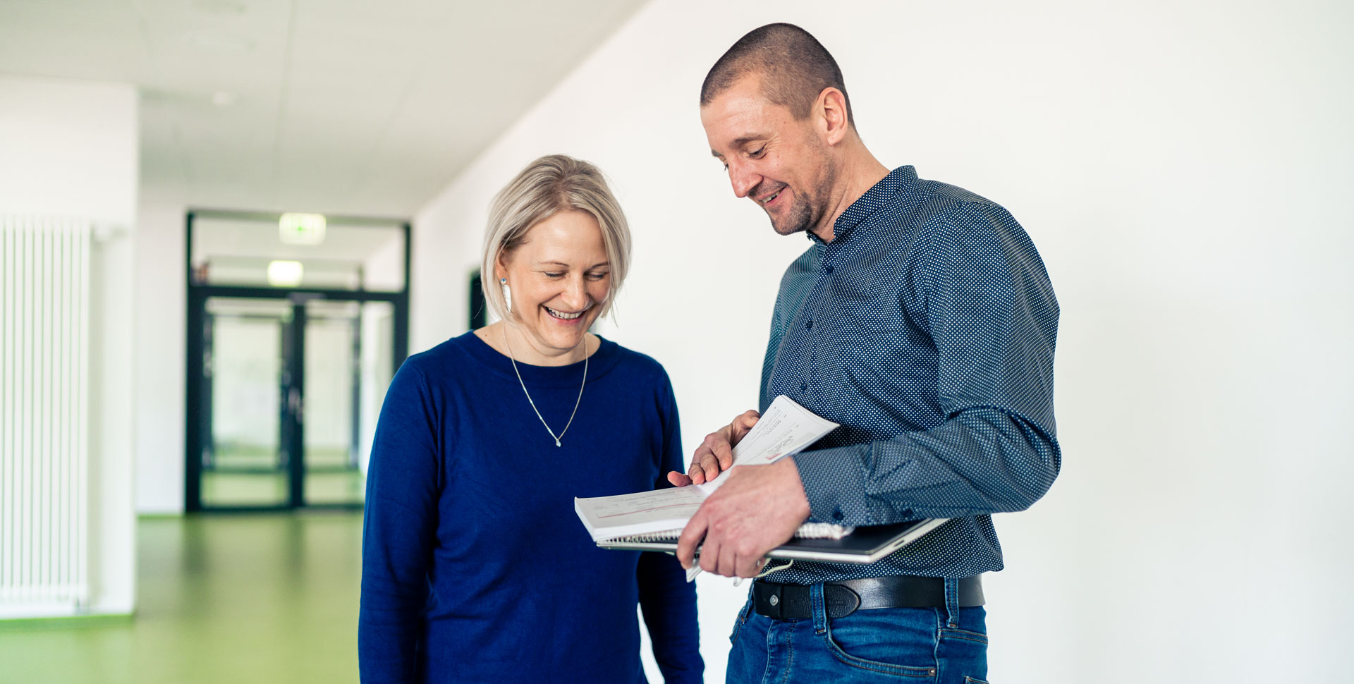Zwei Lehrer stehen im Flur einer Schule und betrachten gemeinsam Unterlagen.