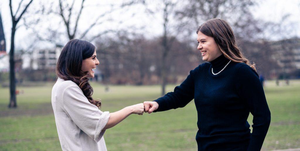 Zwei Frauen, die sich im Freien die Hände geben und lächeln, während sie miteinander sprechen.
