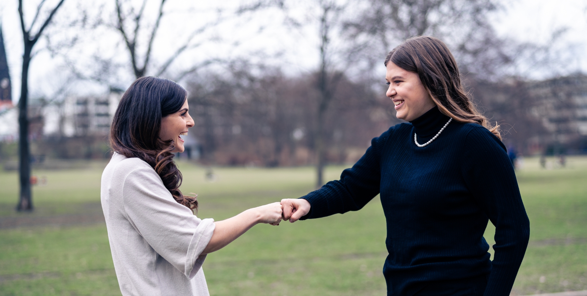 Zwei Frauen, die sich im Freien die Hände geben und lächeln, während sie miteinander sprechen.
