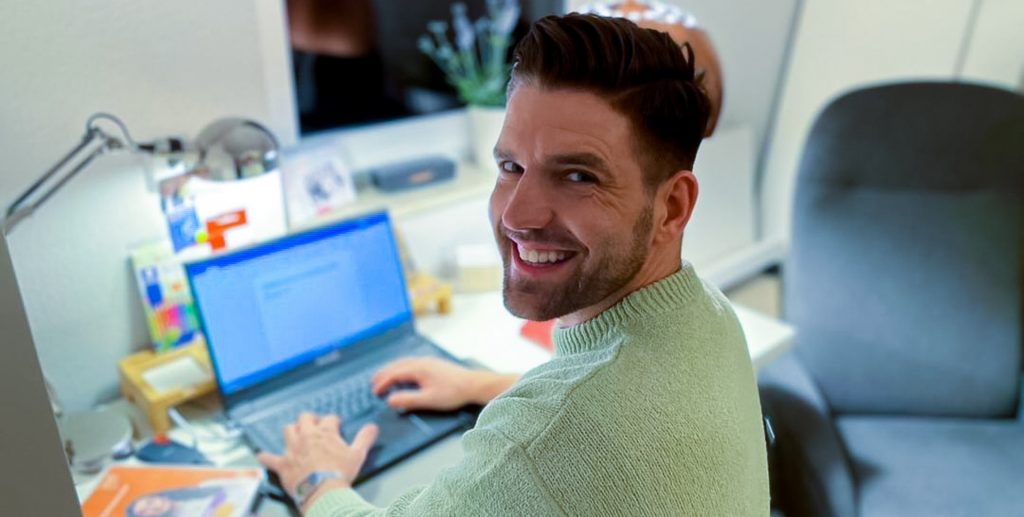 Mann mit kurzem Haar sitzt an einem Schreibtisch und tippt auf einem Laptop.