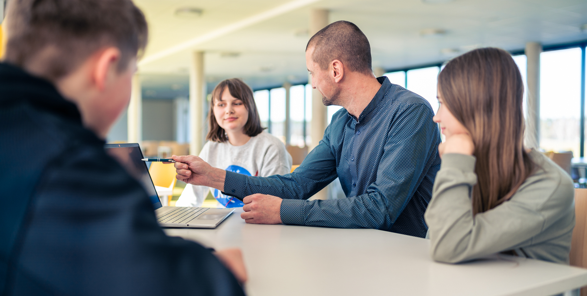 Lehrer zeigt Schülern auf einem Laptop während einer Unterrichtsstunde in einem modernen Raum.