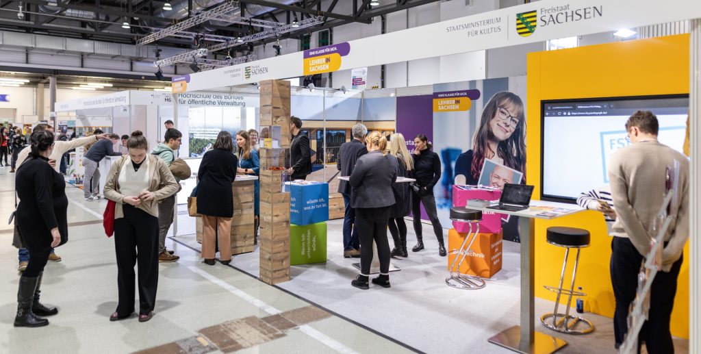 Menschen in einem Messebereich mit verschiedenen Ständen und Informationsmaterialien.