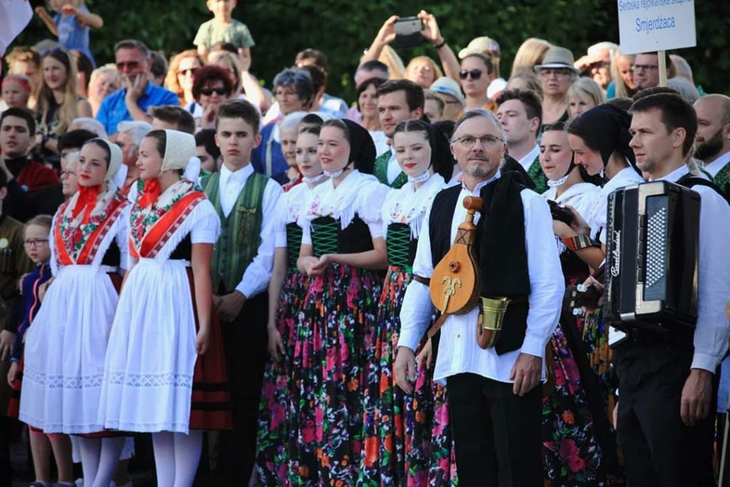 Gruppe von Menschen in traditioneller Tracht während eines Festumzugs, einige mit Instrumenten.