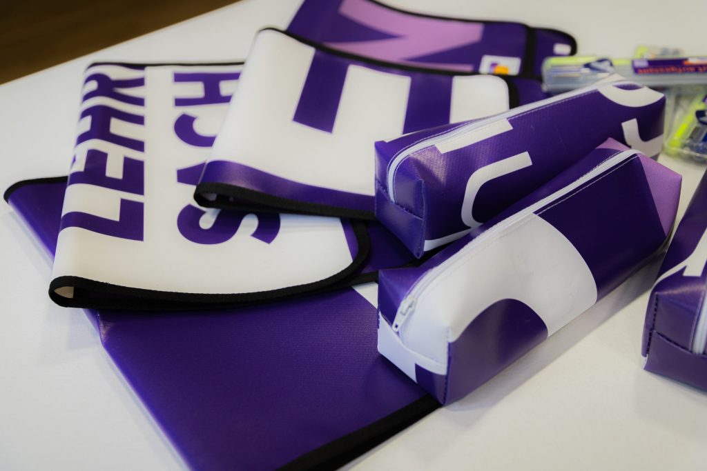 Verschiedene lila und weiße Schreibwaren mit Text auf einer Tischoberfläche angeordnet.