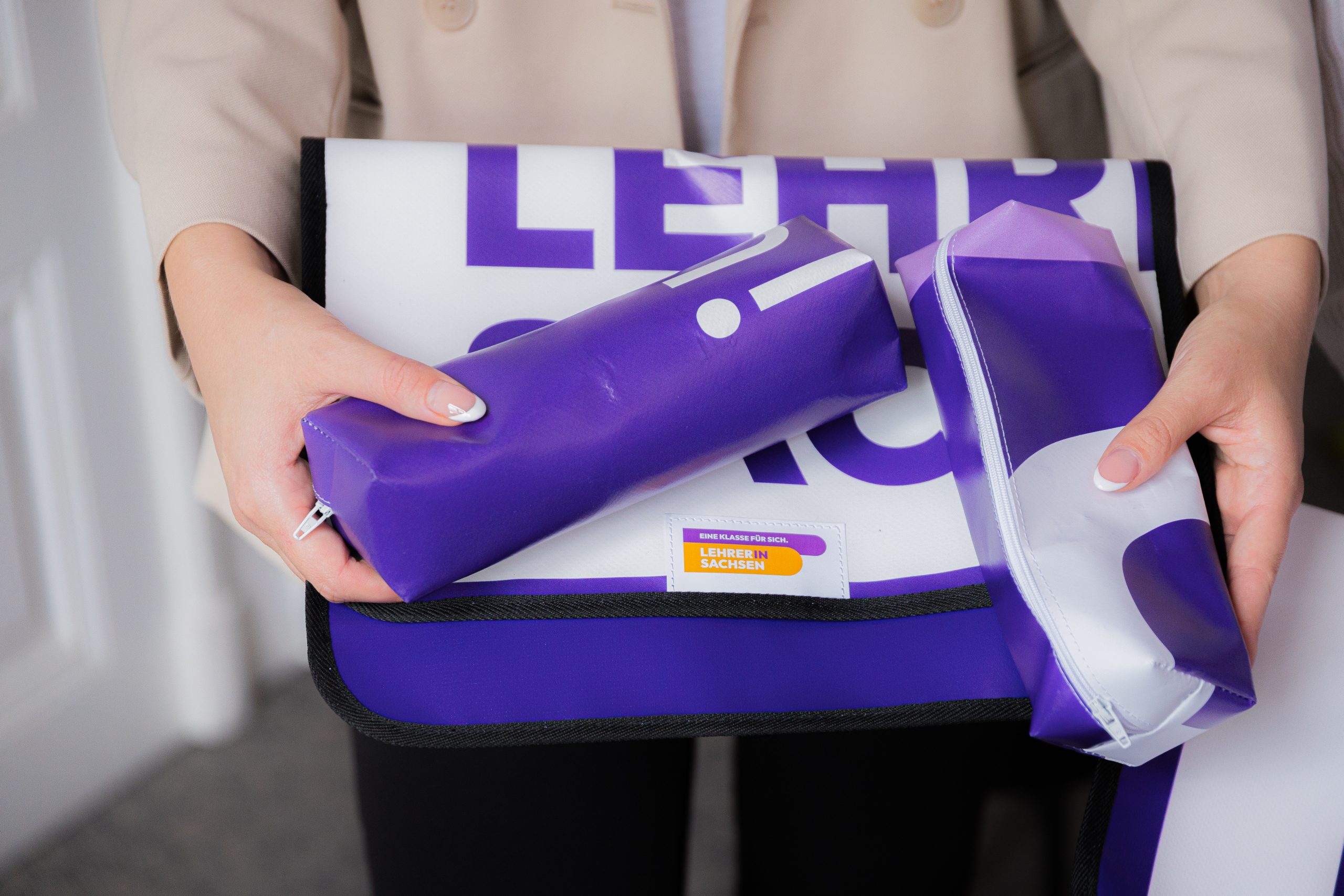 Person hält eine lila Tasche mit zwei passenden Zubehörteilen in den Händen.