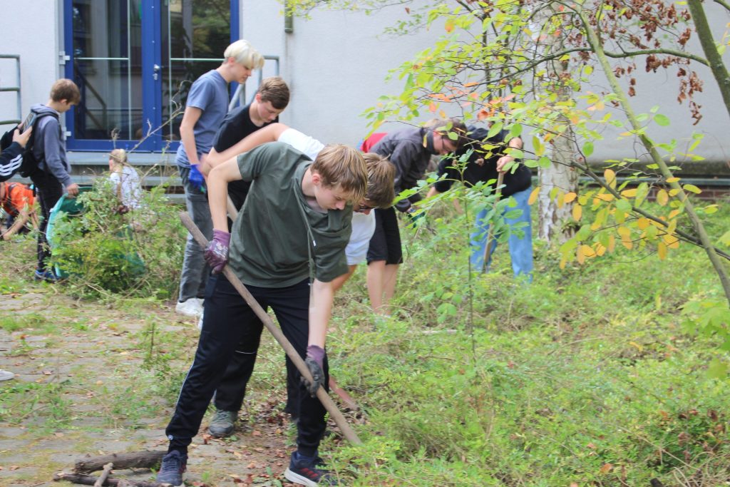 Gruppe von Schülern, die im Freien mit Werkzeugen im Garten arbeiten.