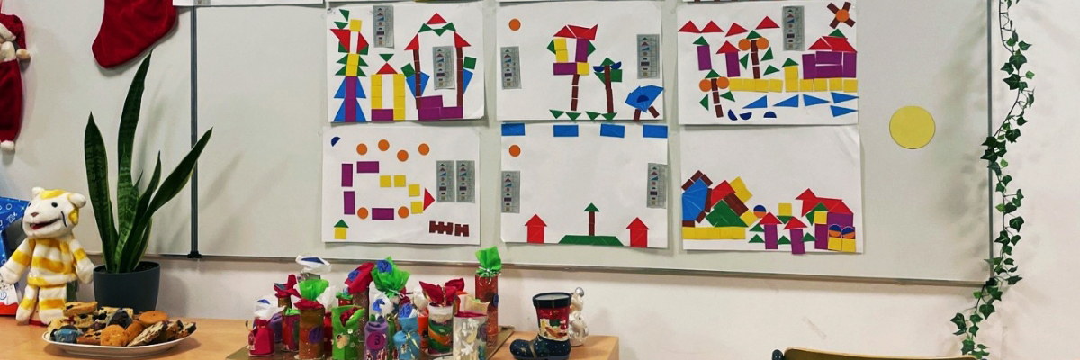 Bunte geometrische Bastelarbeiten an einer Wand im Klassenzimmer mit verschiedenen Formen und Farben.