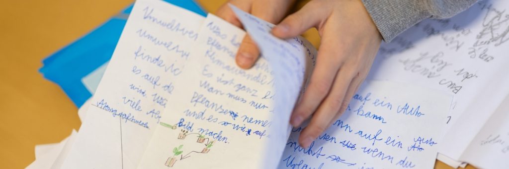 Hände, die mehrere Blätter Papier mit handschriftlichen Notizen und Zeichnungen halten.